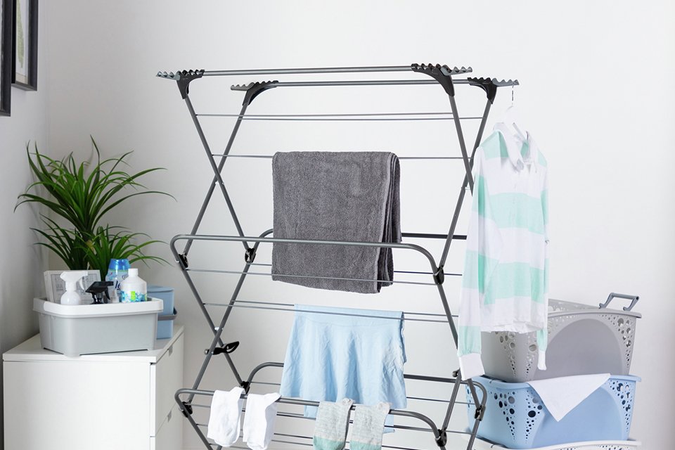 A 3 tier extra wide indoor clothes airer in black placed in a unitlity room next to 3 laundry baskets.